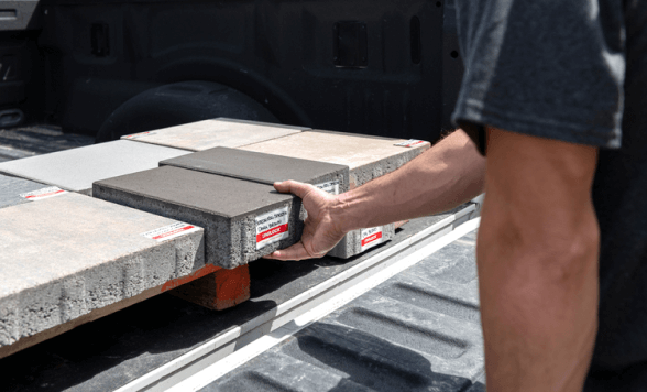 a man picking up a patio stone from the back of a truck 